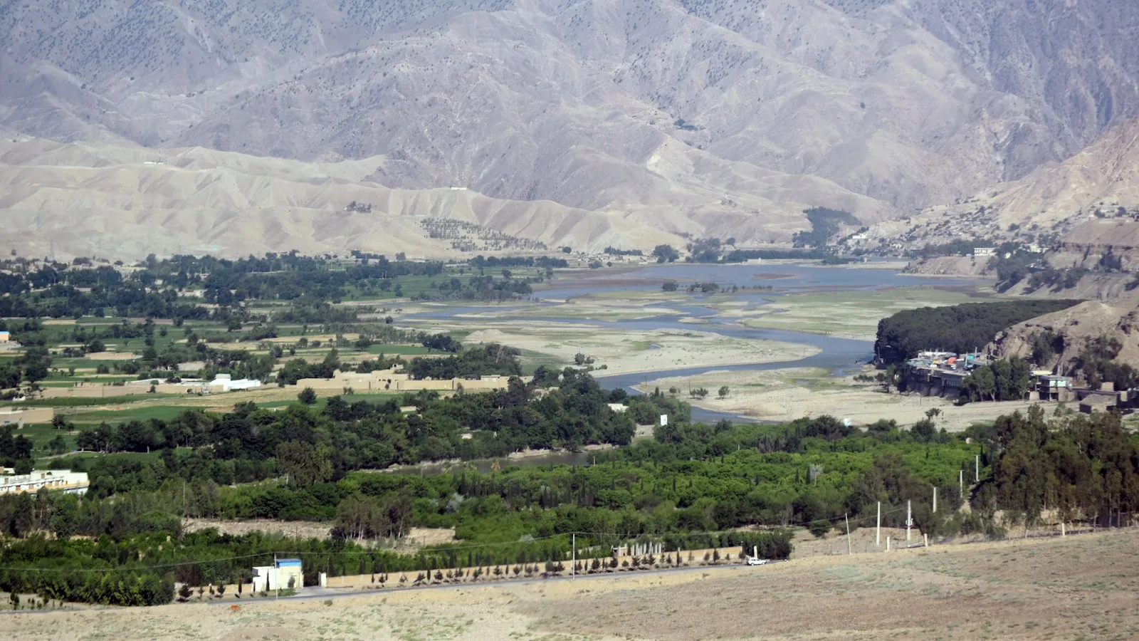 A scenic view of a valley with a lake and mountains in the background
