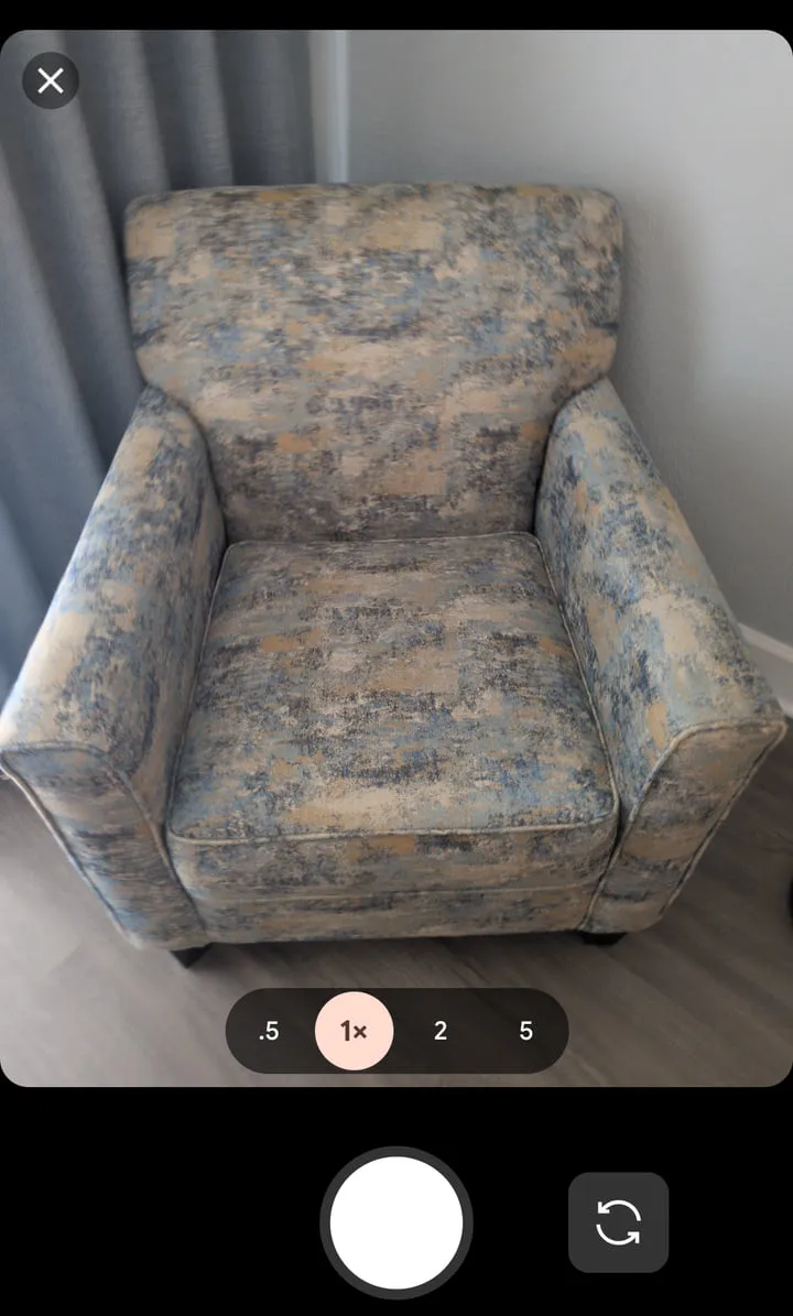 The Yembo capture screen on a phone, framing an upholstered armchair in the camera view with zoom and shutter controls below it.