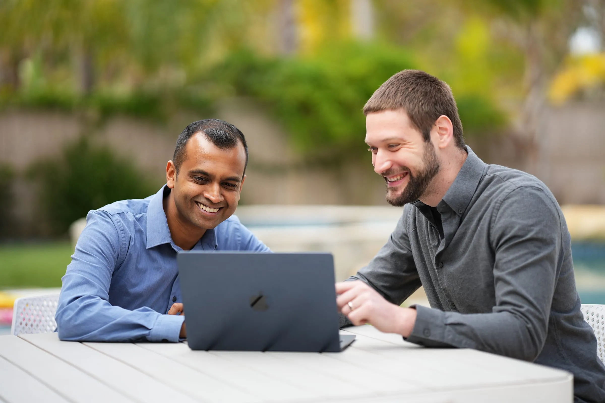Yembo co-founders Siddharth Mohan and Zach Rattner smiling at a laptop screen at an outdoor table.