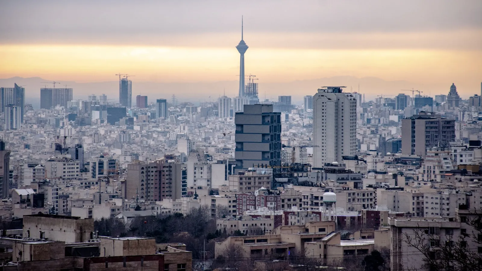 The Tehran skyline at sunset with the Milad Tower rising above the city.