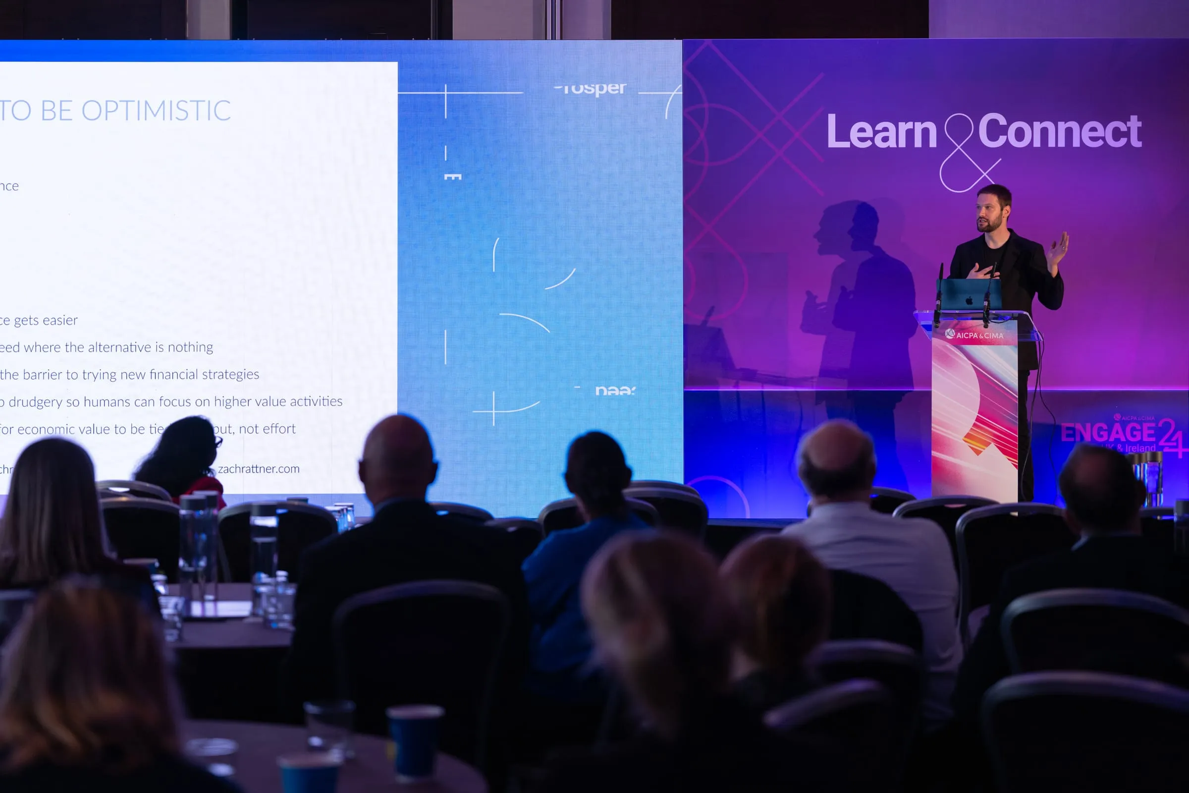 Yembo co-founder and CTO Zach Rattner delivering a keynote from the stage to a seated audience, his slides on the screens beside him.