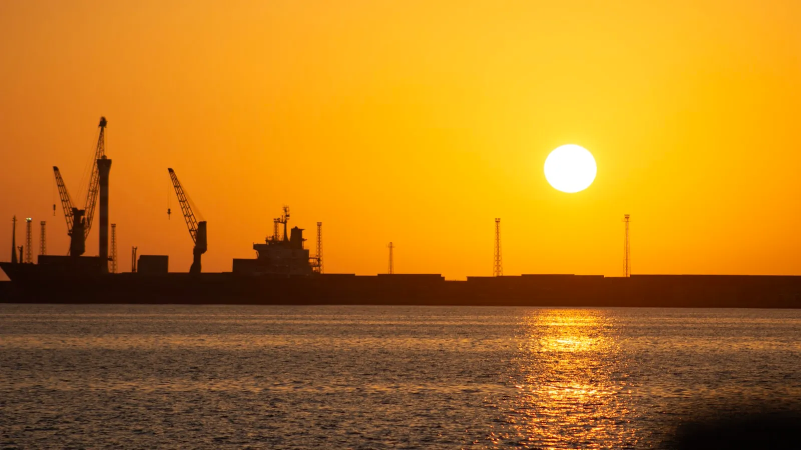 Silhouette of cargo ships and cranes at sunset.