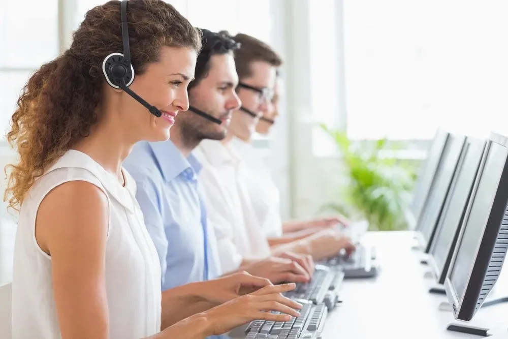 Customer service representatives wearing headsets, working side by side at computers in an office.