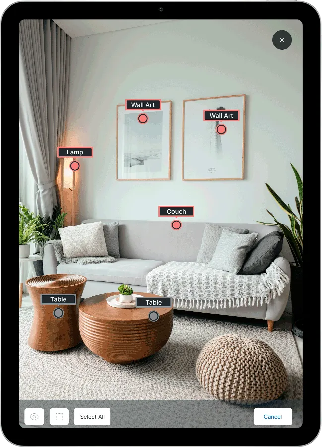 A tablet held up to a living room, with Yembo AI labeling the wall art, lamp, couch, and tables it detects on the live camera view.
