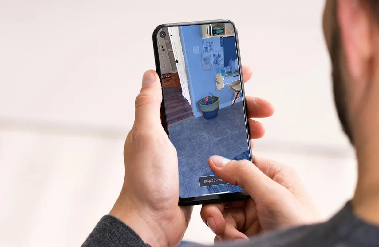 A person holding a phone that shows a bedroom being scanned, with a prompt to stop recording the fourth room.