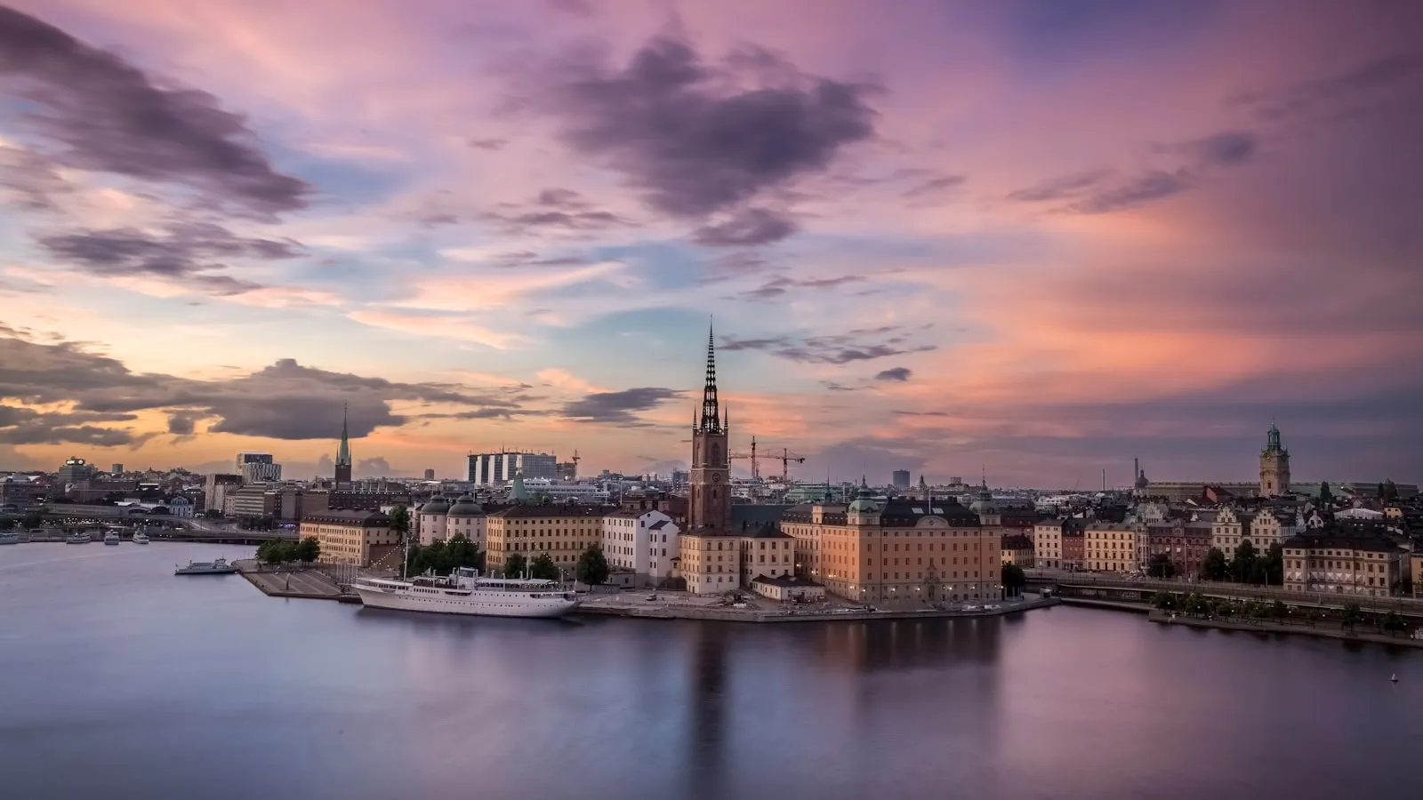 The Riddarholmen Church spire rising above the Stockholm waterfront under a purple sky.