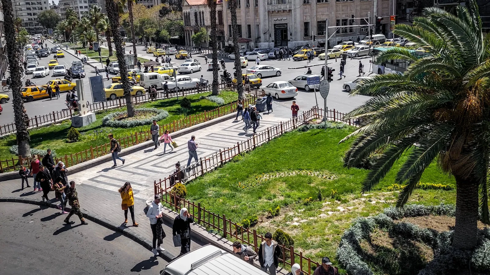A group of people walking down a street next to palm trees