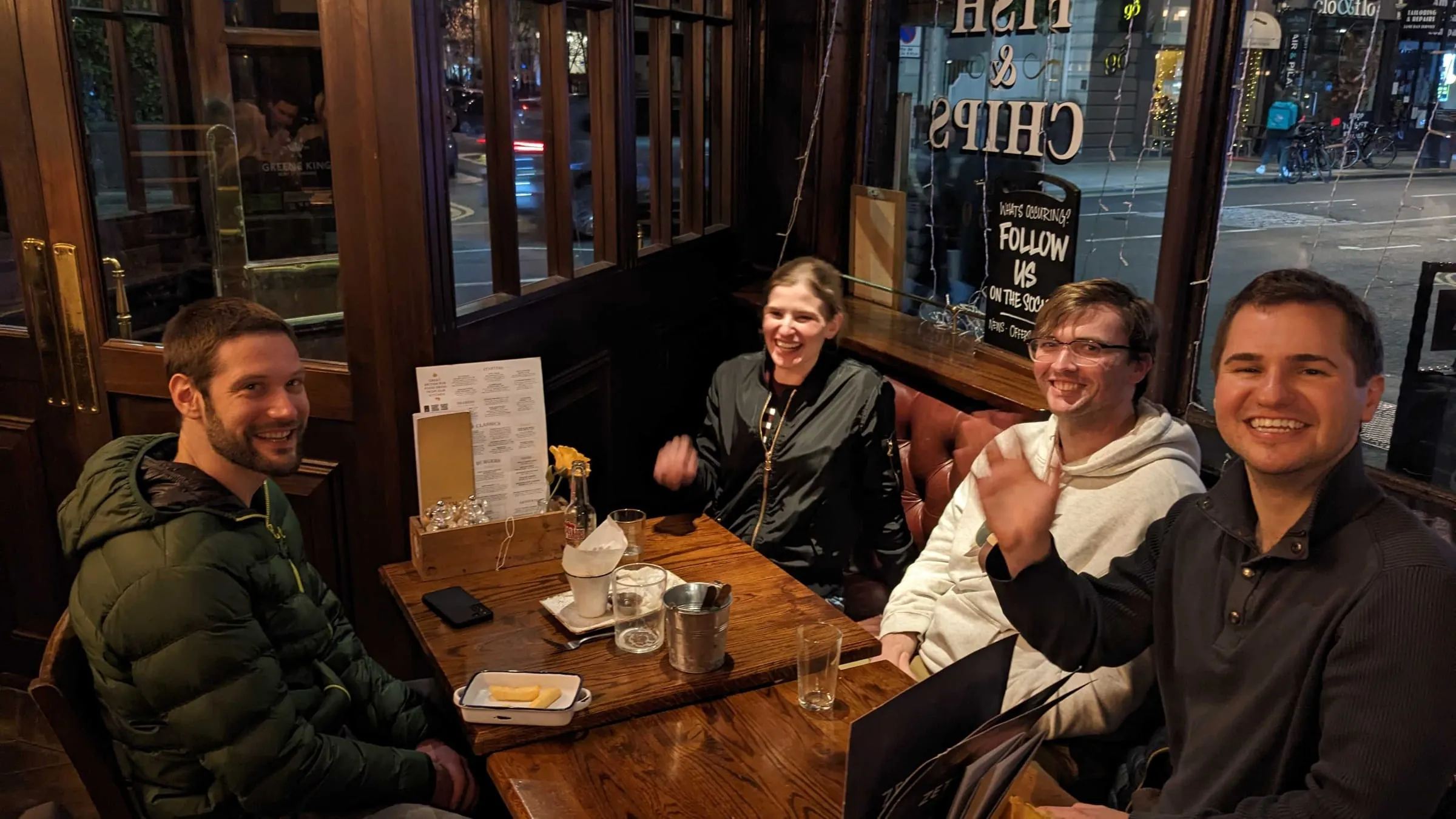 Four members of the team around a corner table at a pub dinner on a work trip, turning to the camera mid-meal.