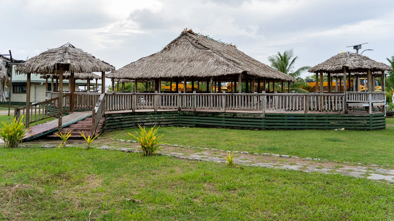 A grassy area with a wooden walkway and thatched huts