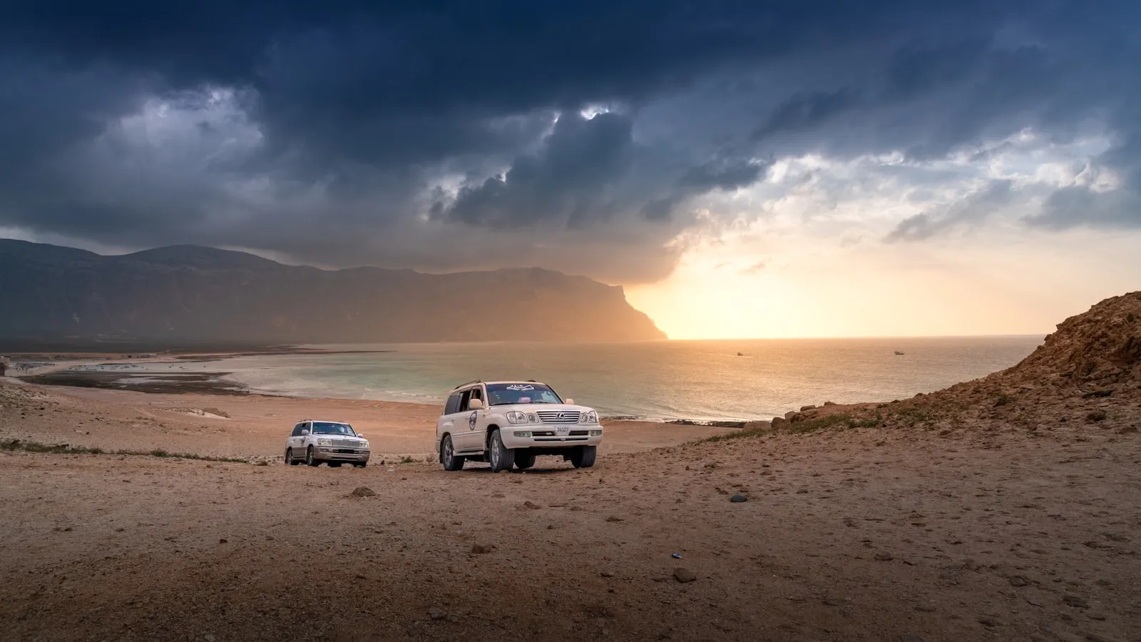 A couple of cars parked on top of a sandy beach